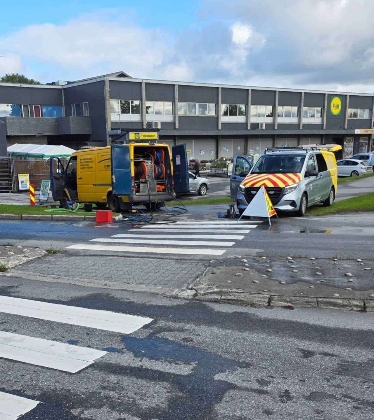 Gul servicebil og en varselmerket bil parkert ved et gangfelt under et oppdrag i gata