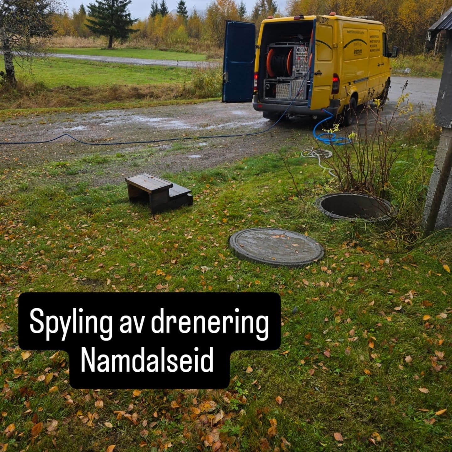Gul spylebil på en gårdsplass med kumlokk i gresset under spyling av drenering